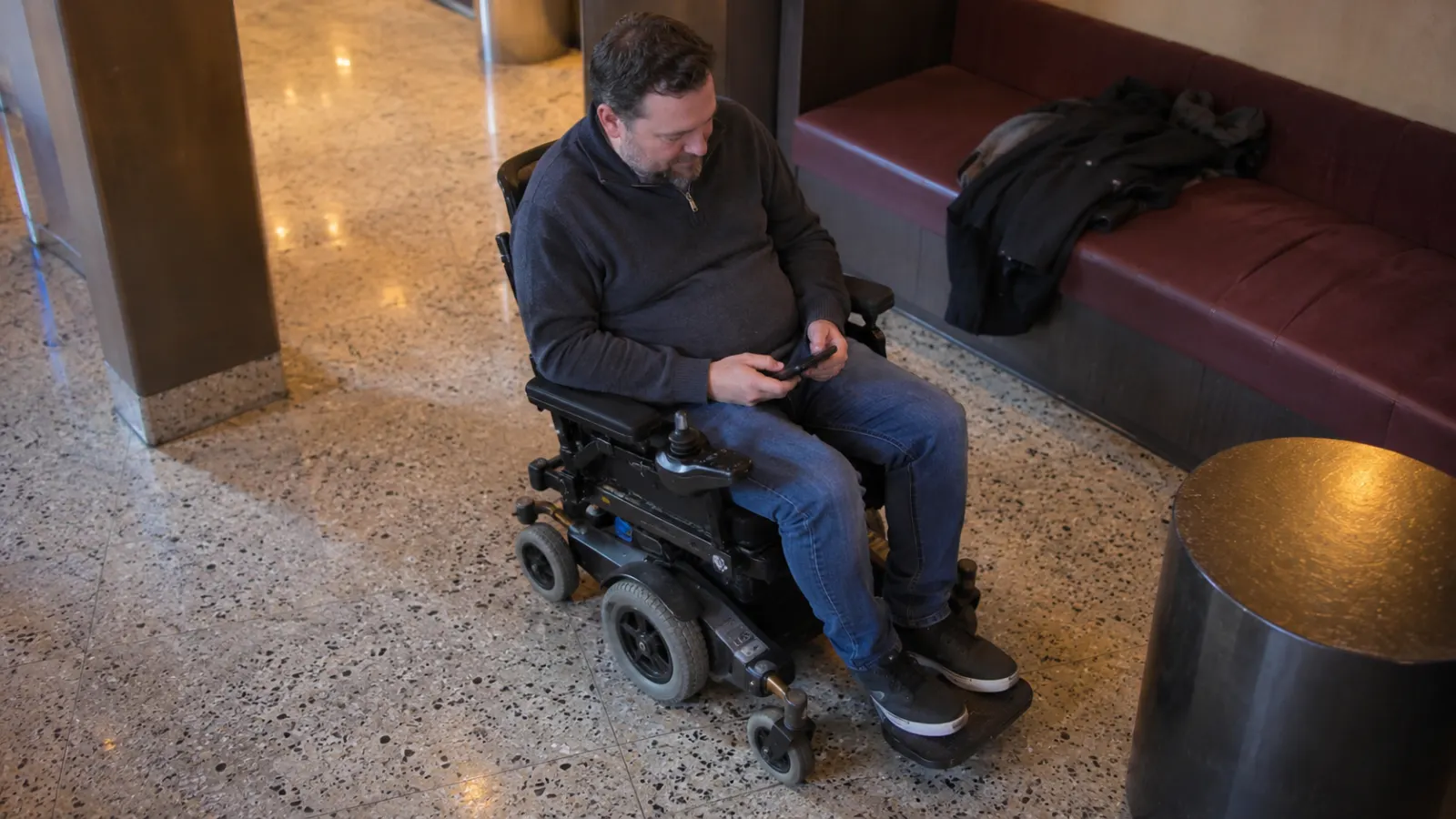 A power wheelchair user checks a phone in a venue lounge.