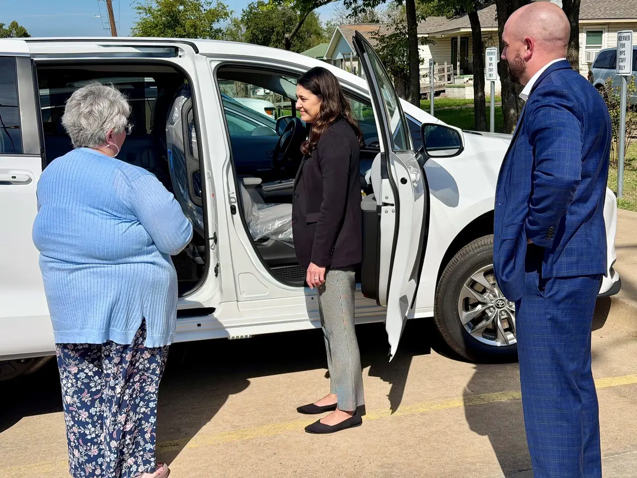 Trois personnes se tiennent à côté d'un minivan blanc aux portes coulissantes ouvertes sur un parking, inspectant l'intérieur du véhicule.