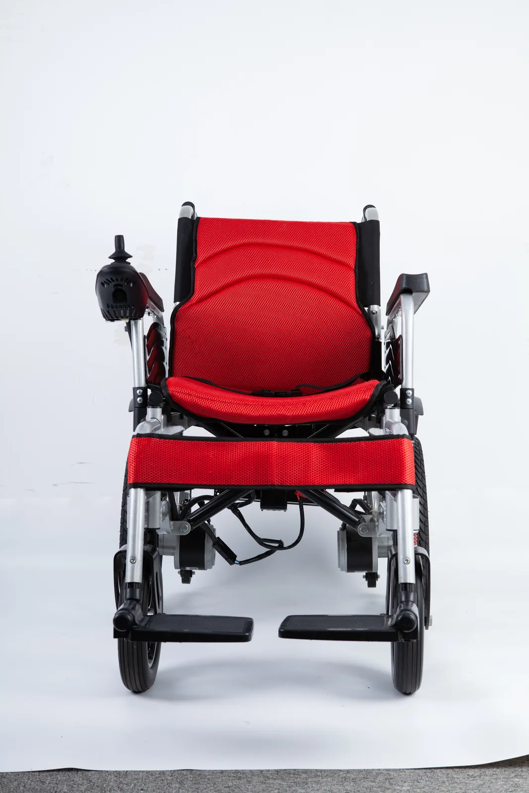 Front view of a red electric wheelchair featuring a mesh seat, silver metal frame, black footrests, and joystick control on the left armrest.
