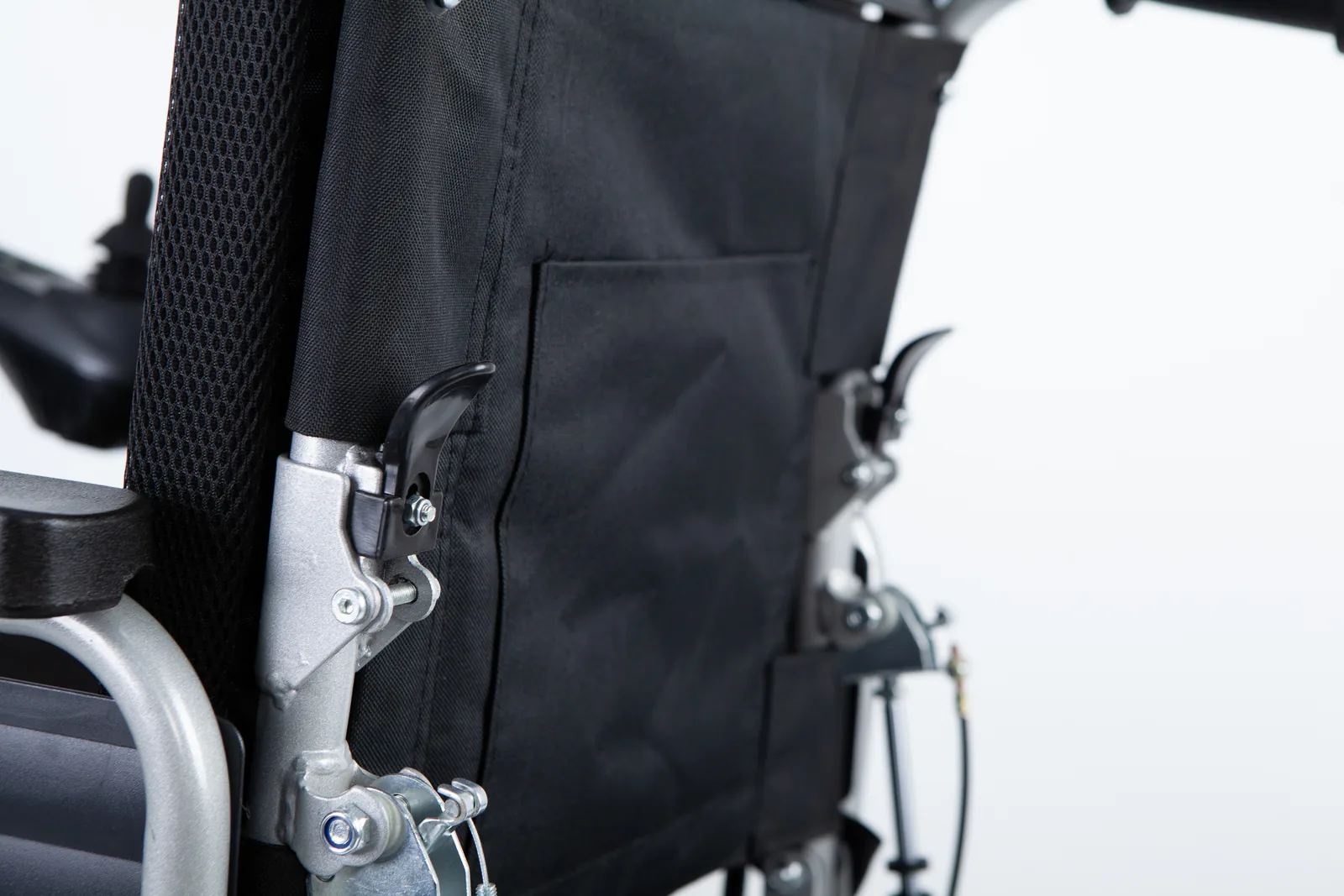 Close-up of the black mesh backrest, silver metal folding latch with a black lever, and rear storage pocket on an electric wheelchair frame.