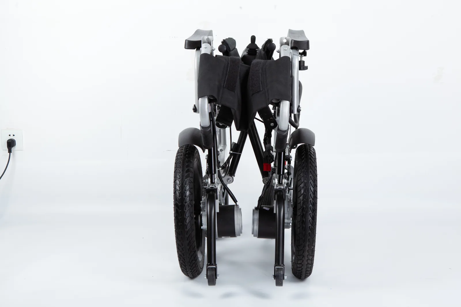 Rear view of a folded silver electric wheelchair with black high-back upholstery, large rear tires, and wheel motors against a white background.
