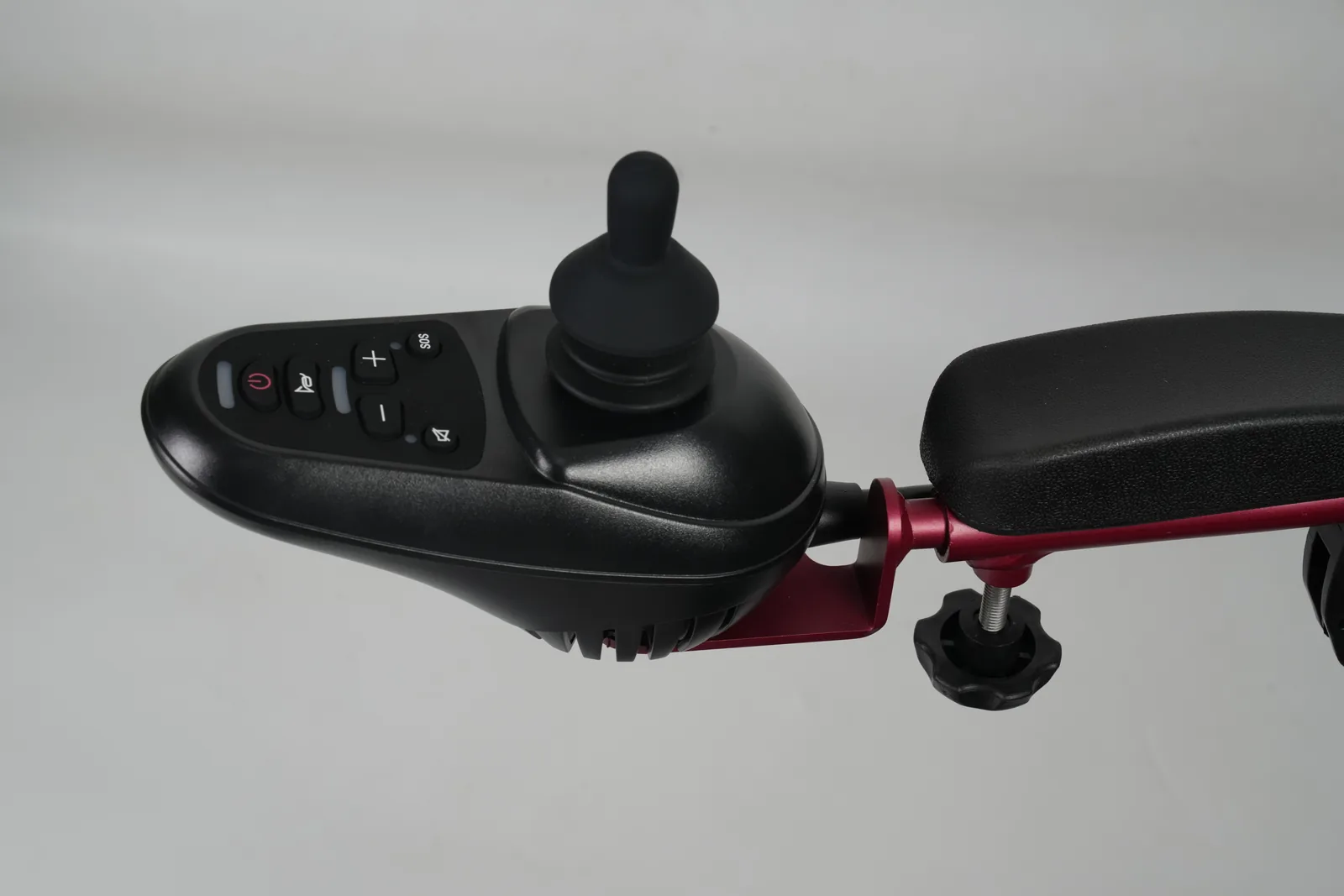 Black joystick controller mounted on a red armrest, featuring buttons for power, horn, speed adjustment, SOS, and sound.